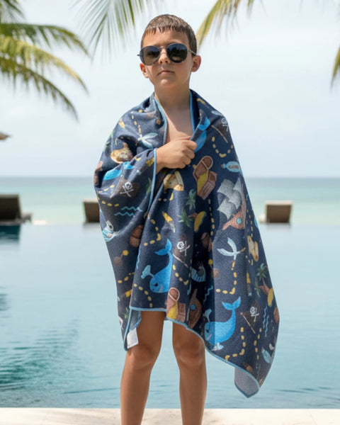Child wrapped in a colorful pirate themed towel with a pool in the background 