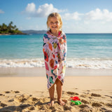 Child wrapped in a colorful fish pattern towel on a sandy beach