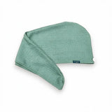 A sage green waffle hair towel wrap with a small dark blue brand tag, shown on a clean white background.