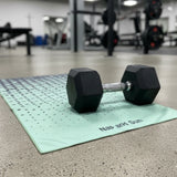 Green gym towel is on the floor of the gym with a dumbbell.