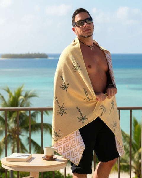 Man wrapped in a yellow towel with palm tree design by the ocean
