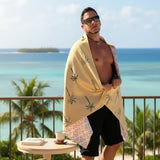 Man wrapped in a yellow towel with palm tree design by the ocean