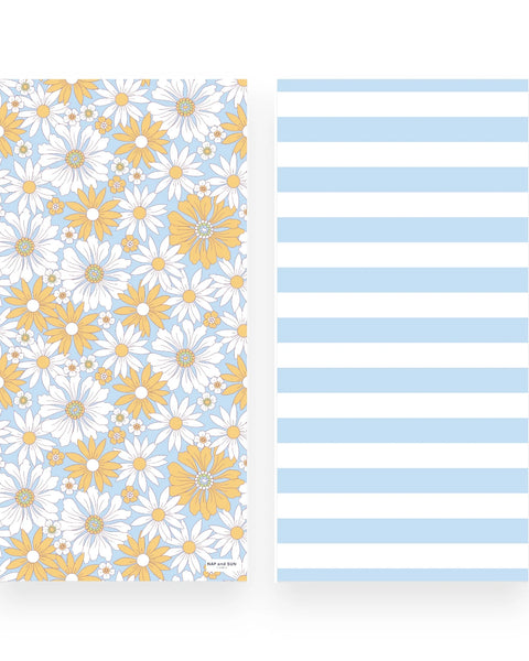A beach towel  front and back sides shown side by side on a white background: the left has a floral print with white daisies and yellow flowers on a light blue ground, and the right has wide light blue and white horizontal stripes.