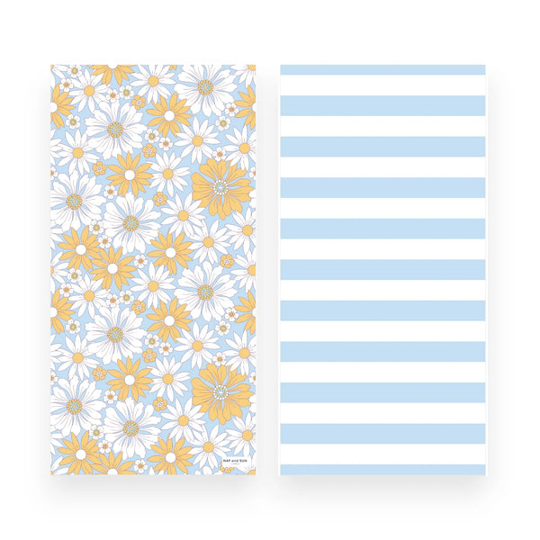 A beach towel  front and back sides shown side by side on a white background: the left has a floral print with white daisies and yellow flowers on a light blue ground, and the right has wide light blue and white horizontal stripes.