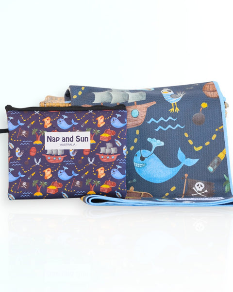 Napandsun Treasure Island sand-free beach towel for kids featuring a pirate-themed design with whales, islands, treasure map, and pirate ships on a dark blue background.  Matching wet bag is included. 