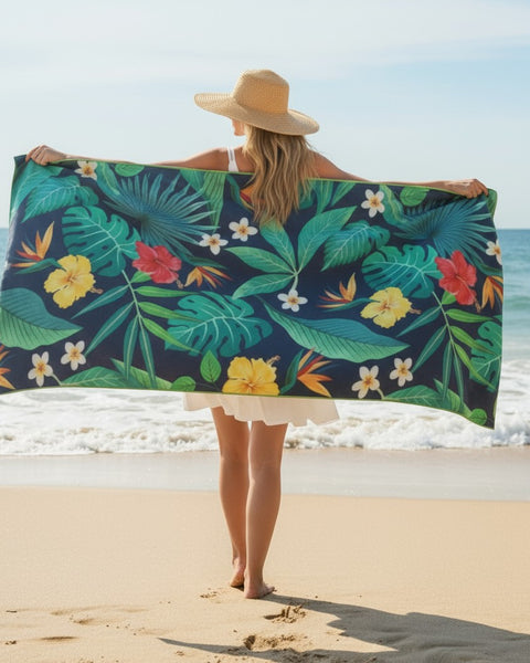 Woman stretching out a tropical-pattern towel on the beach under bright sunlight.