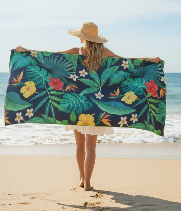 Woman stretching out a tropical-pattern towel on the beach under bright sunlight.