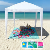 White cabana on a sandy beach with a colorful flower pattern beach mat and picnic setup.