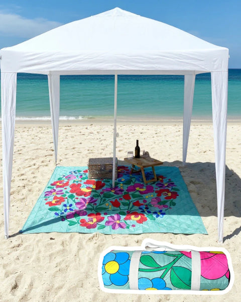 White cabana on a sandy beach with a colorful flower pattern beach mat and picnic setup.