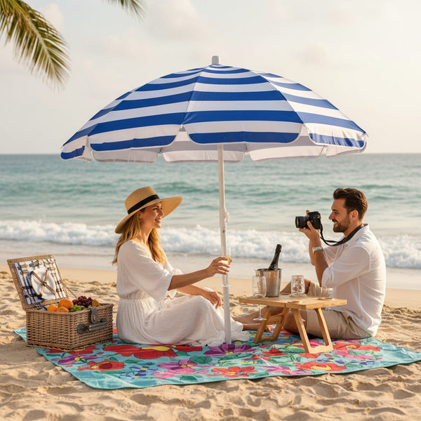 Couple on a beach with an umbrella, picnic basket, and colorful blanket.