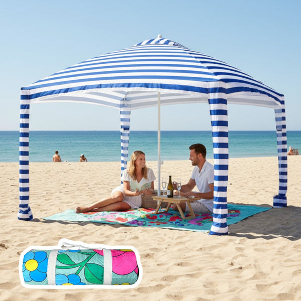 Vivid floral pattern picnic blanket adn attached cabana with people sitting on it on a beach.