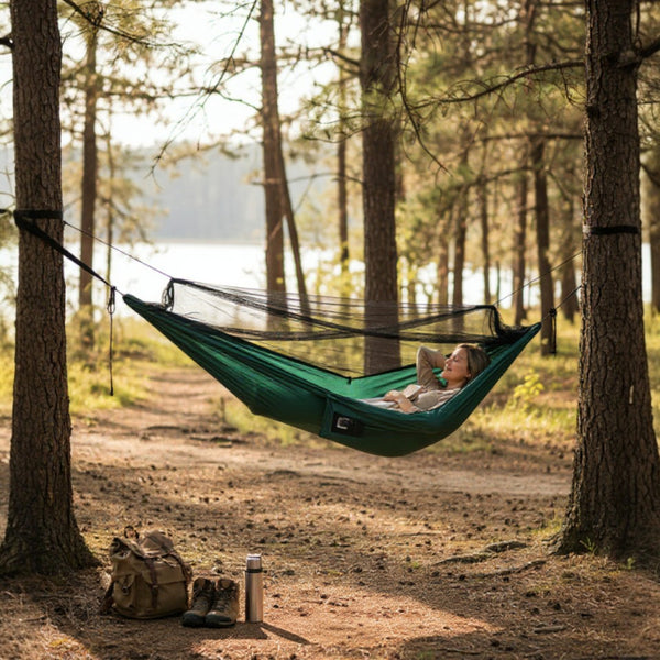 Person relaxing in a green bug net hammock between two trees in a forest.