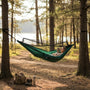 Person relaxing in a green bug net hammock between two trees in a forest.