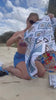Video of a woman unfolding the Azzure towel on the beach and sitting on it, showcasing its XL size, sand-free, and quick-dry features.