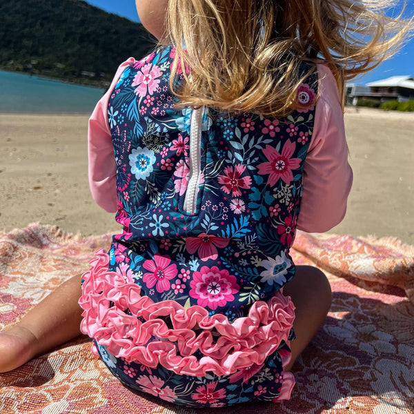 Child wearing a floral swimsuit with ruffles on a beach